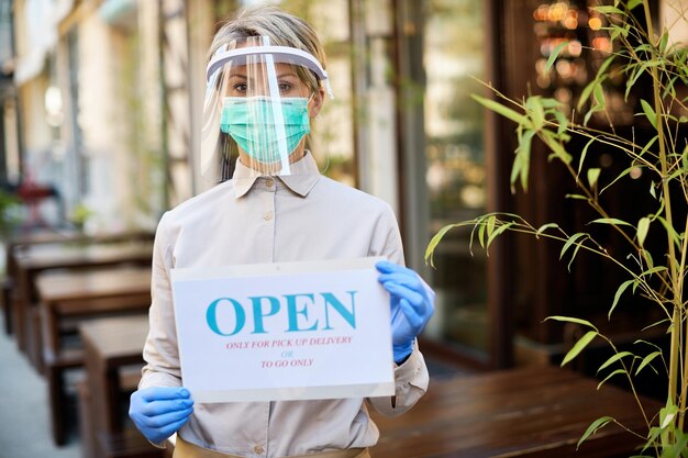 코로나바이러스 전염병으로 인해 테이크아웃 또는 배달 픽업을 위해 열린 표지판을 들고 있는 여성 소유자
