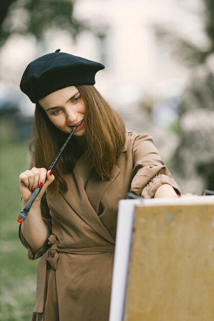 公園で絵を描く女性画家。カーキ色のドレスと黒い帽子をかぶった女性