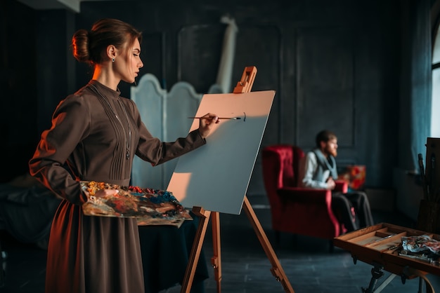 Female painter paints man portrait in art studio