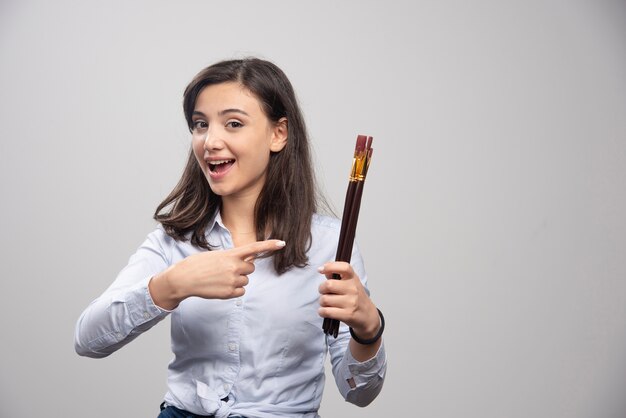 Female painter pointing at paintbrushes on gray wall. 