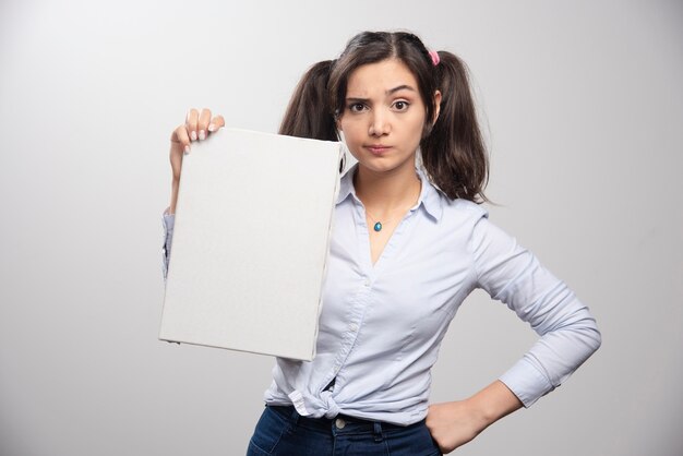 Female painter with ponytail holding empty canvas on gray wall. 