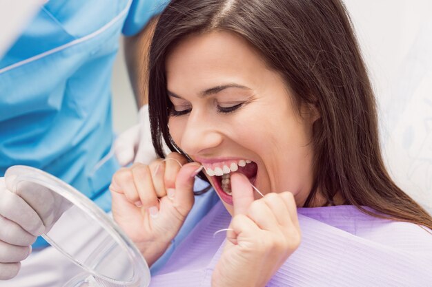 Женский пациент зубной нитью зубы