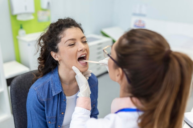 Female patient opening her mouth for the doctor to look in her throat Otolaryngologist examines sore throat of patient