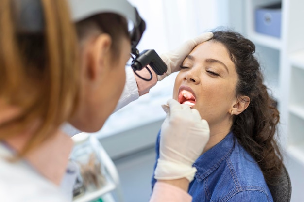 Female patient opening her mouth for the doctor to look in her throat Otolaryngologist examines sore throat of patient