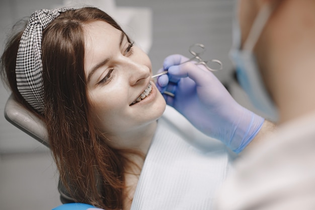 교정기를 착용한 여성 환자는 치과에서 치과 검사를 받습니다. 파란색 장갑을 끼고 구강 전문의