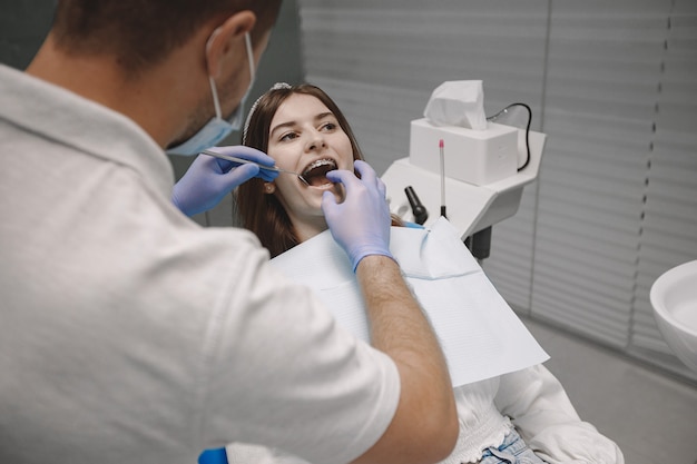 교정기를 착용한 여성 환자는 치과에서 치과 검사를 받습니다. 흰 옷을 입은 여자