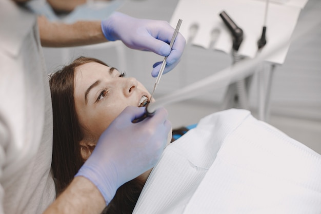 Пациентка с брекетами проходит стоматологическое обследование в кабинете стоматолога. Женщина в белой одежде