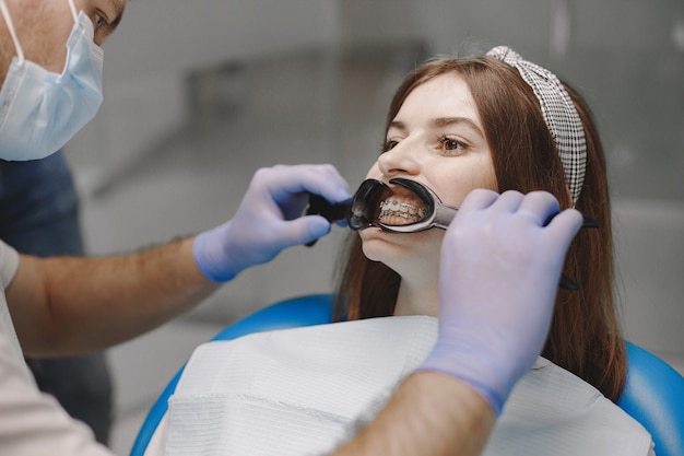 Пациентка с брекетами проходит стоматологическое обследование в кабинете стоматолога. Женщина в белой одежде