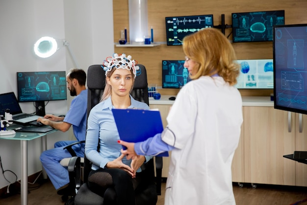 Foto gratuita paziente di sesso femminile con dispositivo di scansione delle onde cerebrali guardando un blocco per appunti. dottore e donna paziente