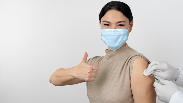 Female patient with medical mask showing thumbs up as she gets vaccine shot