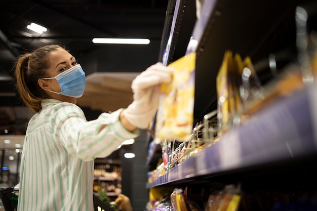 スーパーマーケットで食べ物を買うマスクと手袋を持つ女性