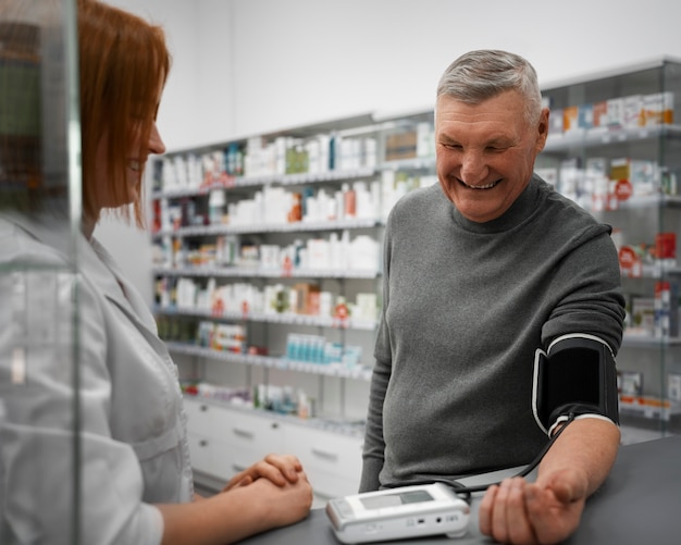 Foto gratuita farmacista femminile che controlla la pressione sanguigna dell'uomo anziano