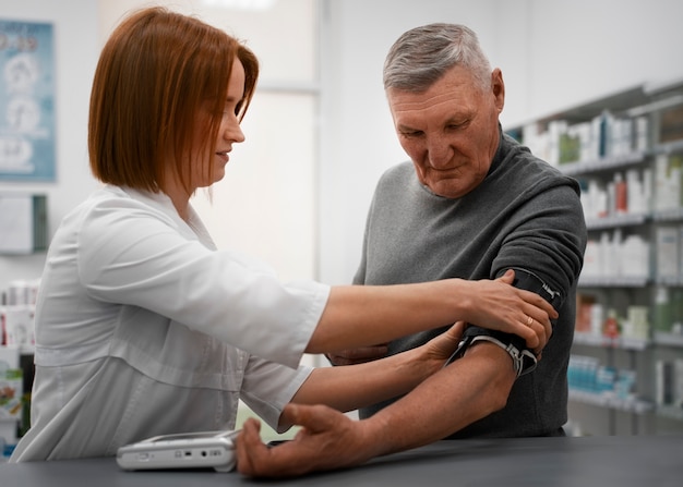 Free photo female pharmacist checking senior man's blood pressure