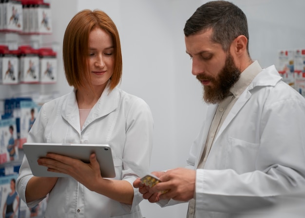 Free photo female pharmacist training male coworker with tablet in the pharmacy