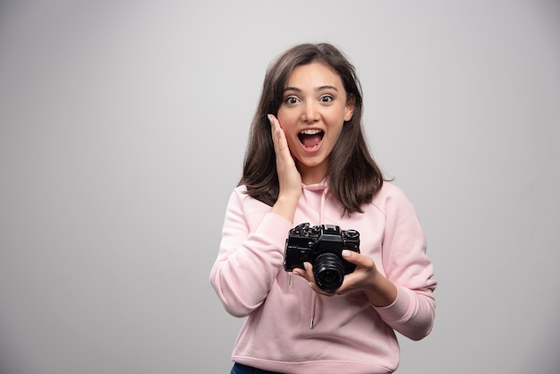 Женский фотограф позирует с камерой на серой стене.