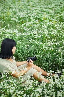 야외에서 카메라를 들고 꽃밭 풍경에 앉아 있는 여성 사진가는 디지털 카메라를 손에 들고 있습니다. 여행 자연 사진, 텍스트를 위한 공간, 평면도.