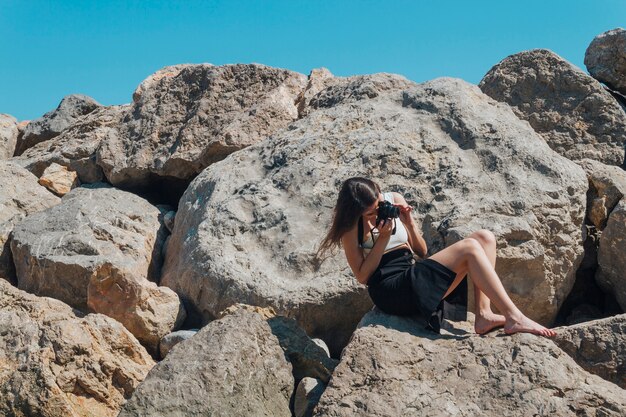 바다 근처 카메라로 바위 복용 사진에 앉아 여성 사진 작가