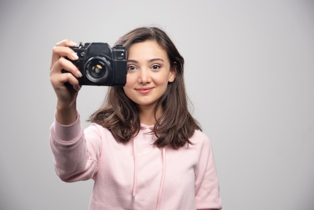 Female photographer taking her photo on gray wall. 