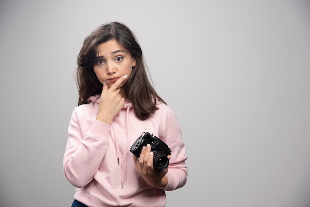 Female photographer with camera standing on gray wall.