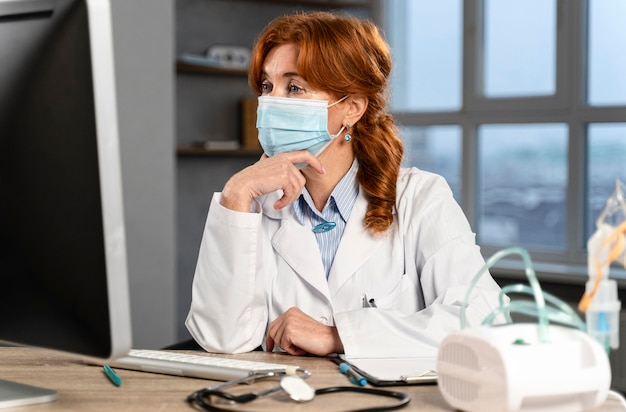 Female physician at her desk with medical mask looking at computer
