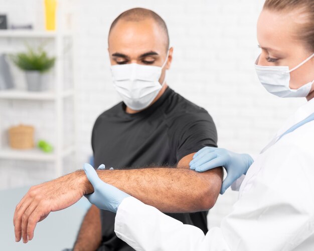 Female physiotherapist with medical mask checking man's elbow