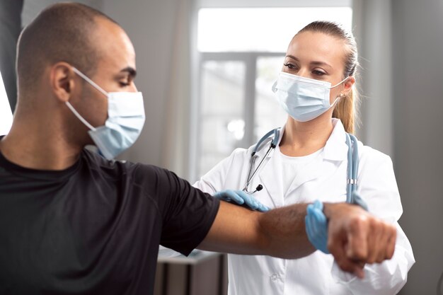 男性の肘をチェックする医療マスクと手袋を持つ女性理学療法士