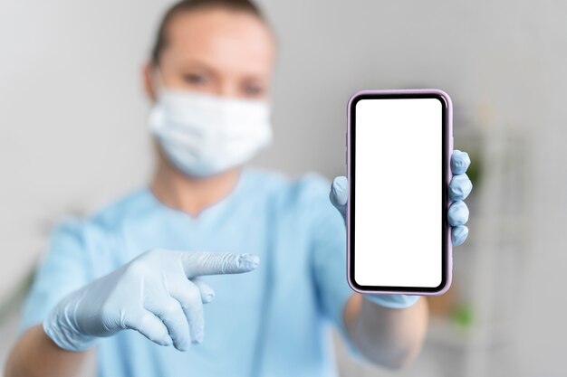 Женский физиотерапевт с медицинской маской, указывая на смартфон