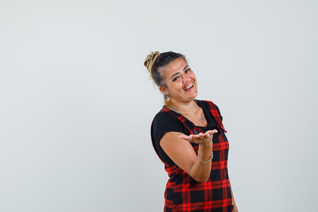 Female in pinafore dress pretending to hold or offer something and looking happy , front view.