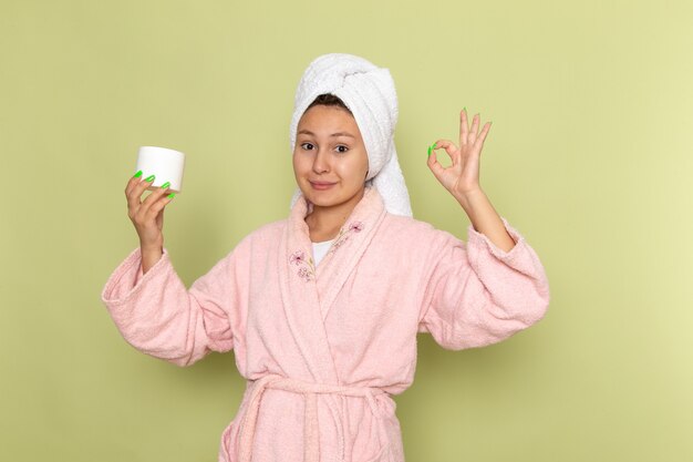 female in pink bathrobe holding cream for face