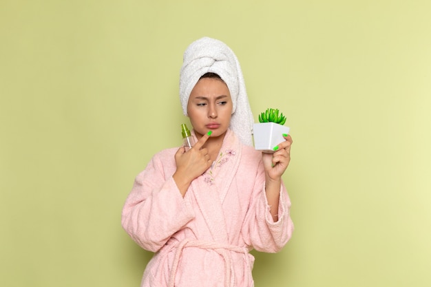 female in pink bathrobe holding spray flask and plant