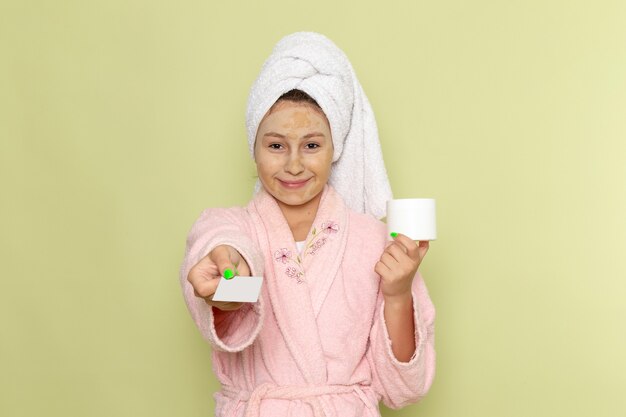 female in pink bathrobe holding white card and cream