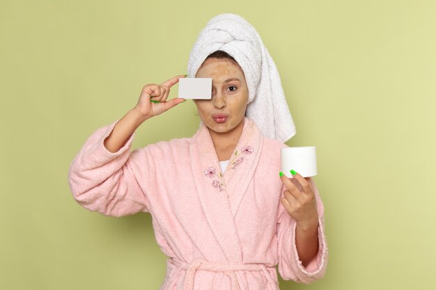 female in pink bathrobe holding white card and cream