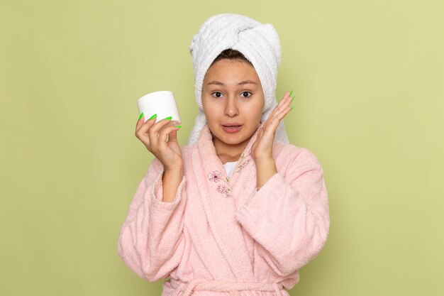 female in pink bathrobe holding white cream