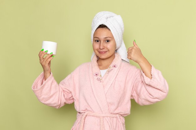 female in pink bathrobe smiling and holdign white cream