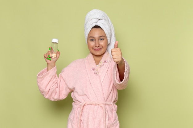 female in pink bathrobe with smile on her face holding spray flask
