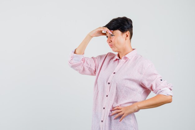 Female in pink shirt rubbing forehead and looking sad , front view.