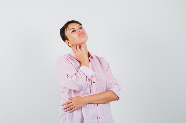 Female in pink shirt scratching neck and looking hesitant , front view.