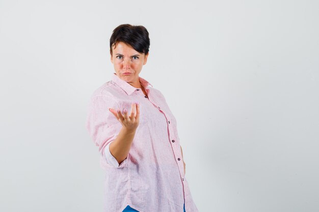 Женщина в розовой рубашке, протягивая руку озадаченным жестом, вид спереди.