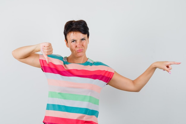 Free photo female pointing aside, showing thumb down in striped t-shirt and looking displeased , front view.