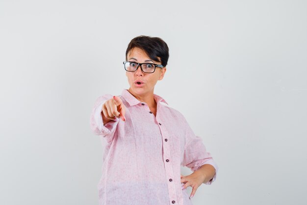 Female pointing at camera in pink shirt and looking surprised. front view.