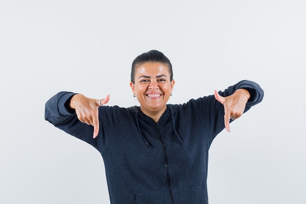 Free photo female pointing down in hoodie and looking happy. front view.