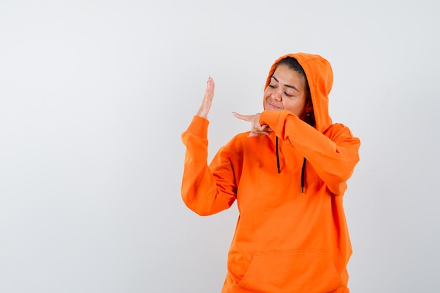 Free photo female pointing at her empty palm in orange hoodie and looking confident