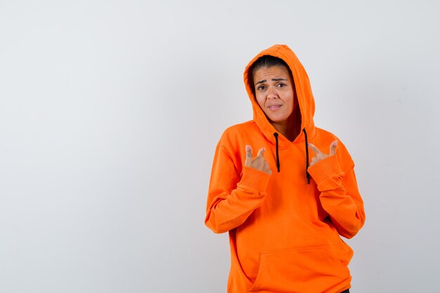 Female pointing at herself in orange hoodie and looking puzzled 