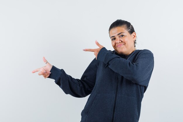 Female pointing to the left side in hoodie and looking confident. front view.