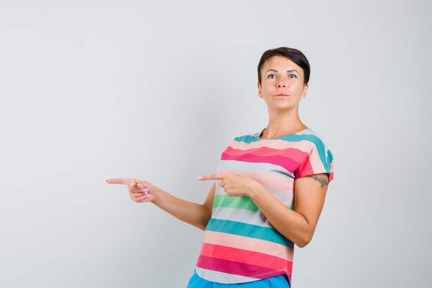 Female pointing to the side in striped t-shirt, pants and looking hesitant , front view.