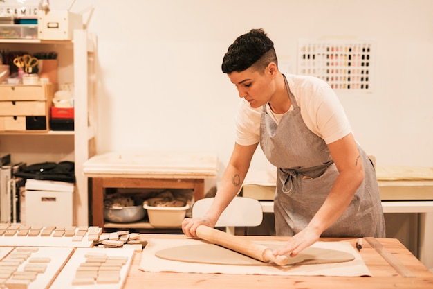 Female potter flattening the clay with rolling pin on wooden table