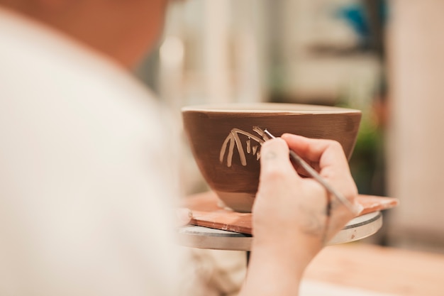 Female potter's hand decorating the clay bowl with tool