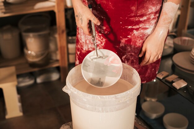 Free photo female potter's hand painting the ceramic plate in the workshop