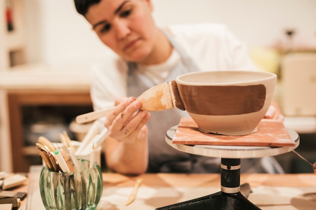女性の陶工のペイントブラシで粘土ボウルを塗る