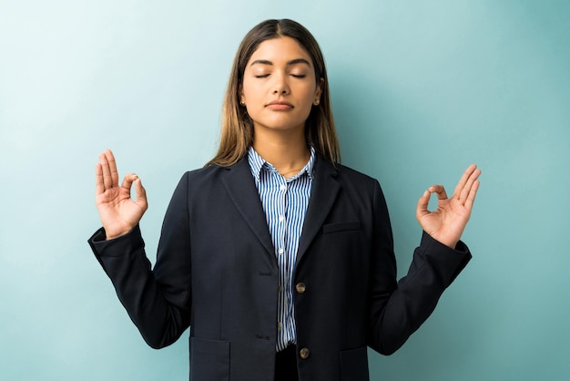 Female professional in suit gesturing while meditating against isolated background